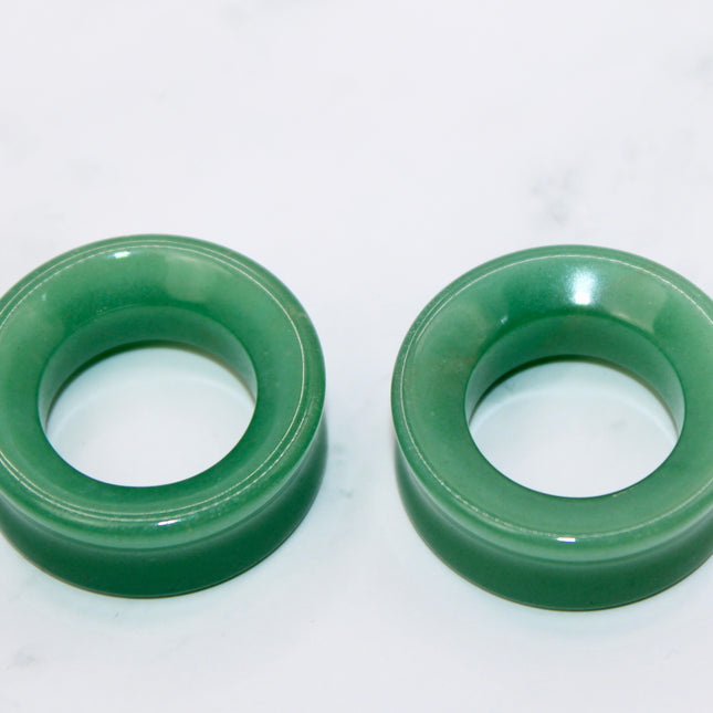 Two green aventurine tunnel plugs on a white marble surface