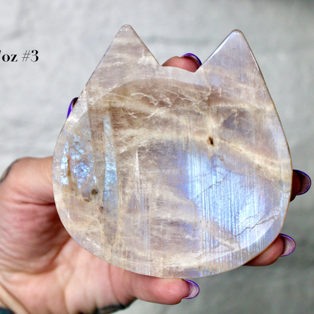 This Moonstone Bowl is carved from natural stone and polished to reveal stunning blue flash across its surface. Its compact size and elegant shine make it both functional and decorative ideal for adding a touch of iridescence to any space