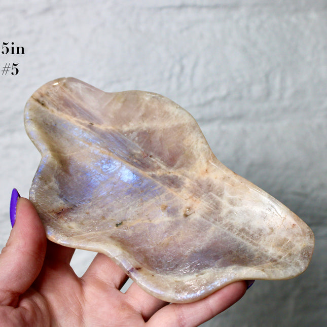 This Moonstone Bowl is carved from natural stone and polished to reveal stunning blue flash across its surface. Its compact size and elegant shine make it both functional and decorative ideal for adding a touch of iridescence to any space