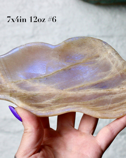 This Moonstone Bowl is carved from natural stone and polished to reveal stunning blue flash across its surface. Its compact size and elegant shine make it both functional and decorative ideal for adding a touch of iridescence to any space