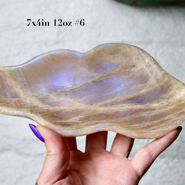 This Moonstone Bowl is carved from natural stone and polished to reveal stunning blue flash across its surface. Its compact size and elegant shine make it both functional and decorative ideal for adding a touch of iridescence to any space