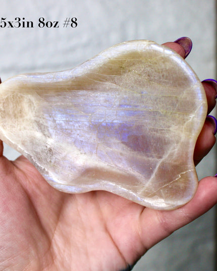 This Moonstone Bowl is carved from natural stone and polished to reveal stunning blue flash across its surface. Its compact size and elegant shine make it both functional and decorative ideal for adding a touch of iridescence to any space