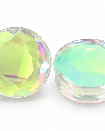 Two round, faceted clear glass plugs with an iridescent, holographic finish, one standing vertically and the other lying horizontally, on a white background.