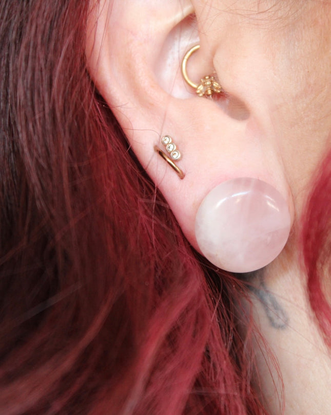 A beautifully polished pair of Rose Quartz Double Flare Plugs rests delicately on a pale surface, their soft pink tones glowing in natural light. Each plug features the gentle, translucent hue that rose quartz is known for—ranging from milky blush to faint petal pink, with subtle natural marbling throughout. The smooth, glossy finish highlights the stone’s calming energy, while the double flare design ensures a secure, comfortable fit for stretched ears. 