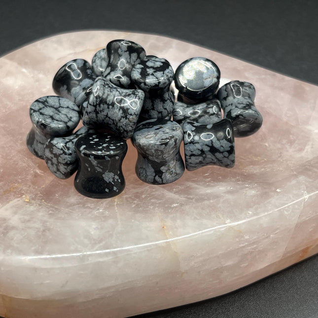 These Snowflake Obsidian Double Flared Plugs feature a smooth, polished surface with natural gray-white crystal "snowflakes" scattered across a rich black volcanic glass base. The double flare ensures a secure, comfortable fit for stretched ears without the need for O-rings. Each pair is uniquely patterned, showcasing the stone’s natural beauty and grounding energy. Durable and stylish, these plugs add a bold yet refined touch to any stretched ear jewelry collection.
