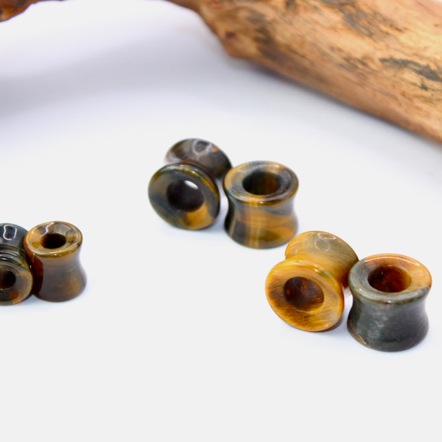 A striking pair of Tiger Eye tunnel plugs, precision-carved and polished to a smooth, glossy finish. These double flare tunnels feature the signature golden-brown hues and shimmering chatoyancy that Tiger Eye is known for, with each piece showcasing unique natural banding and depth. The hollow center adds a bold visual dimension while keeping the plugs lightweight and breathable for stretched ears. 