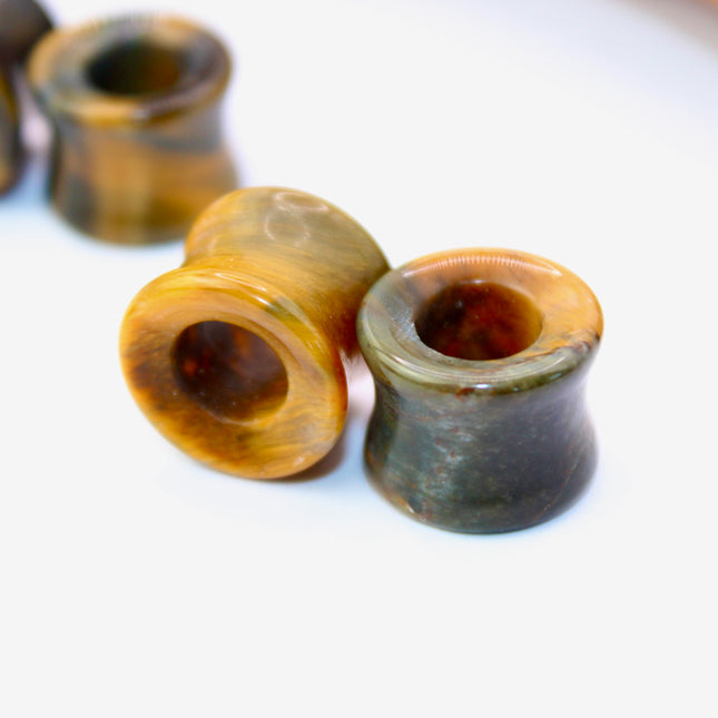 A striking pair of Tiger Eye tunnel plugs, precision-carved and polished to a smooth, glossy finish. These double flare tunnels feature the signature golden-brown hues and shimmering chatoyancy that Tiger Eye is known for, with each piece showcasing unique natural banding and depth. The hollow center adds a bold visual dimension while keeping the plugs lightweight and breathable for stretched ears. 