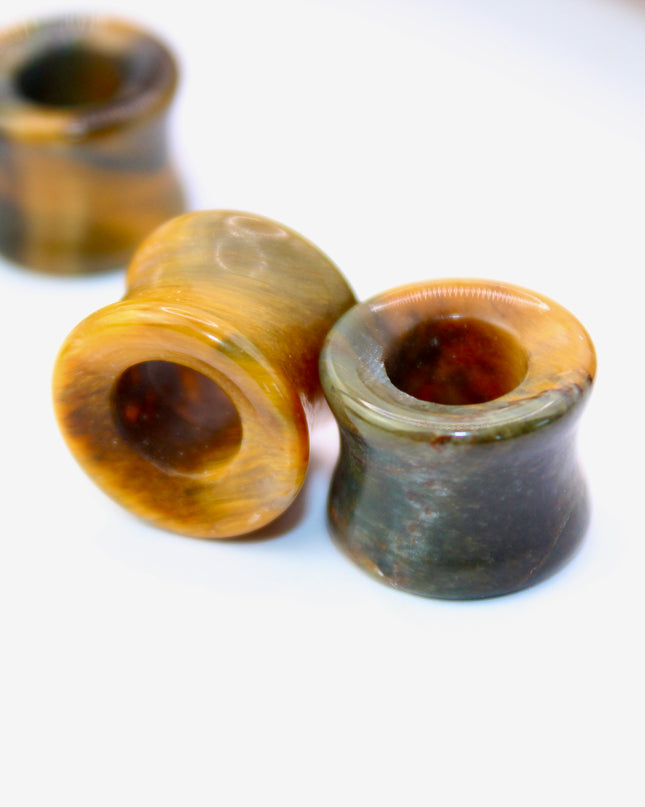 A striking pair of Tiger Eye tunnel plugs, precision-carved and polished to a smooth, glossy finish. These double flare tunnels feature the signature golden-brown hues and shimmering chatoyancy that Tiger Eye is known for, with each piece showcasing unique natural banding and depth. The hollow center adds a bold visual dimension while keeping the plugs lightweight and breathable for stretched ears. 