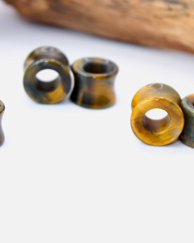 A striking pair of Tiger Eye tunnel plugs, precision-carved and polished to a smooth, glossy finish. These double flare tunnels feature the signature golden-brown hues and shimmering chatoyancy that Tiger Eye is known for, with each piece showcasing unique natural banding and depth. The hollow center adds a bold visual dimension while keeping the plugs lightweight and breathable for stretched ears. 