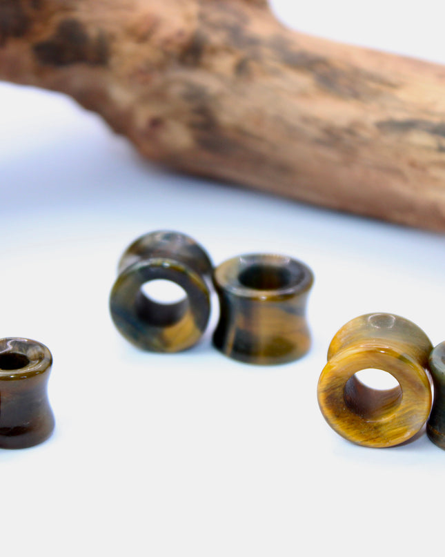 A striking pair of Tiger Eye tunnel plugs, precision-carved and polished to a smooth, glossy finish. These double flare tunnels feature the signature golden-brown hues and shimmering chatoyancy that Tiger Eye is known for, with each piece showcasing unique natural banding and depth. The hollow center adds a bold visual dimension while keeping the plugs lightweight and breathable for stretched ears. 