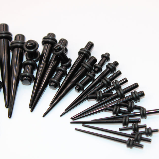 A complete ear stretching kit displayed in size order, featuring black acrylic tapers and matching double flare plugs. The tapers are sleek and lightweight, gradually increasing in size from 14G to 00G, designed to assist with smooth and safe ear stretching. Each size comes with a pair of straight tapers and a matching pair of plugs, all with rounded edges and rubber O-rings for secure placement. The set is neatly arranged to show the full gauge progression, ideal for beginne