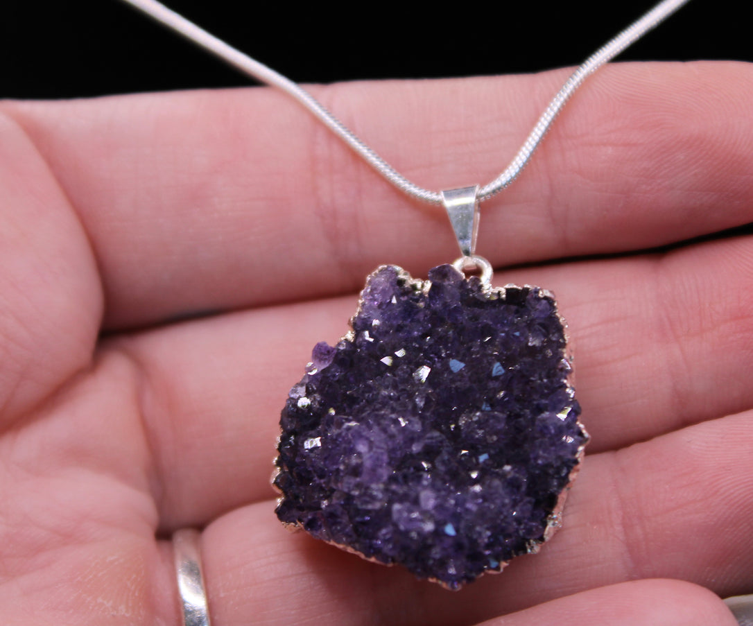 A beautiful Amethyst Pendant hangs gracefully from a sleek silver-color chain, combining natural elegance with everyday wearability. The pendant features a polished amethyst point or cabochon (style can vary), showcasing rich purple hues with subtle marbling or translucence that catches the light. Set in a simple metal cap or loop, the natural stone takes center stage. The silver-tone chain adds a modern, minimalist touch and pairs effortlessly with any outfit. 