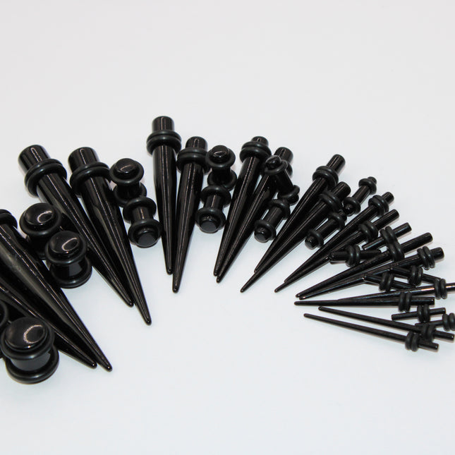 A complete ear stretching kit displayed in size order, featuring black acrylic tapers and matching double flare plugs. The tapers are sleek and lightweight, gradually increasing in size from 14G to 00G, designed to assist with smooth and safe ear stretching. Each size comes with a pair of straight tapers and a matching pair of plugs, all with rounded edges and rubber O-rings for secure placement. The set is neatly arranged to show the full gauge progression, ideal for beginners