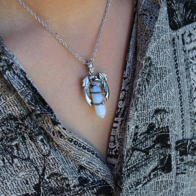 A fierce and enchanting Dragon Necklace with Opalite brings fantasy to life, featuring a detailed dragon wrapped protectively around a glowing opalite orb. The iridescent stone shimmers with soft hues of blue, lavender, and pearly white, catching light with a mystical glow. The dragon pendant is crafted with intricate scales and wings, giving it a bold, medieval-inspired aesthetic.