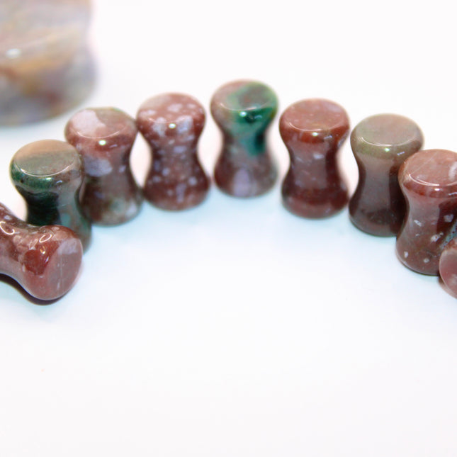 A beautifully varied pair of Rainbow Indian Agate Plugs rests on a natural-toned background, each plug showcasing its own unique mix of earthy colors. From deep forest green and mossy olive to warm rust, cream, and occasional hints of burgundy or gray, the natural banding and marbling of the stone give these plugs a one-of-a-kind character. The polished surface brings out the rich tones and subtle textures of the agate. Shaped with a comfortable, secure double flare, these plugs are perfect for those who ap