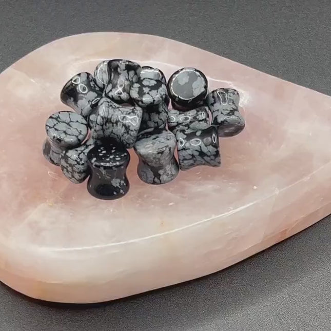 These Snowflake Obsidian Double Flared Plugs feature a smooth, polished surface with natural gray-white crystal "snowflakes" scattered across a rich black volcanic glass base. The double flare ensures a secure, comfortable fit for stretched ears without the need for O-rings. Each pair is uniquely patterned, showcasing the stone’s natural beauty and grounding energy. Durable and stylish, these plugs add a bold yet refined touch to any stretched ear jewelry collection.