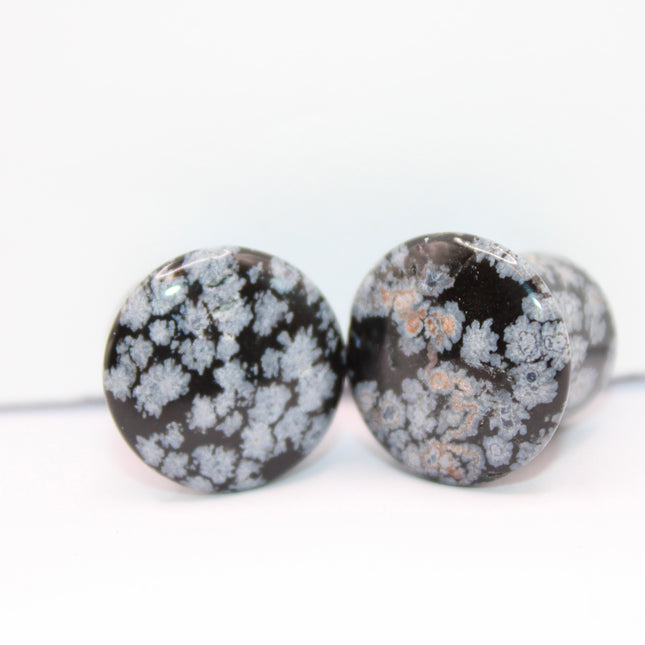 These Snowflake Obsidian Double Flared Plugs feature a smooth, polished surface with natural gray-white crystal "snowflakes" scattered across a rich black volcanic glass base. The double flare ensures a secure, comfortable fit for stretched ears without the need for O-rings. Each pair is uniquely patterned, showcasing the stone’s natural beauty and grounding energy. Durable and stylish, these plugs add a bold yet refined touch to any stretched ear jewelry collection.