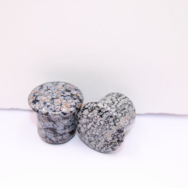 These Snowflake Obsidian Double Flared Plugs feature a smooth, polished surface with natural gray-white crystal "snowflakes" scattered across a rich black volcanic glass base. The double flare ensures a secure, comfortable fit for stretched ears without the need for O-rings. Each pair is uniquely patterned, showcasing the stone’s natural beauty and grounding energy. Durable and stylish, these plugs add a bold yet refined touch to any stretched ear jewelry collection.